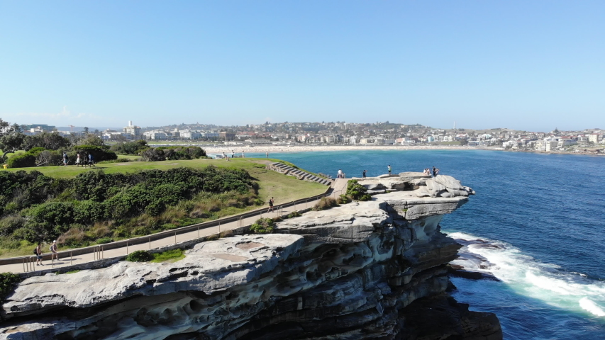 Reverse aerial shot of a stone cliff overlooking the ocean at Coogee Walk.
