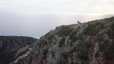Human standing on a huge cliff looking into the ocean at sunset. Flying drone revealing the scale of Gjipe Canyon and the Adriatic Sea.