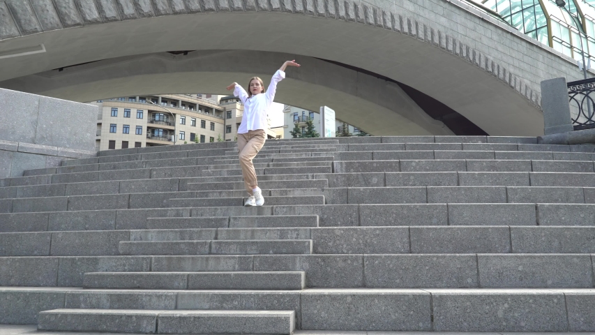 A girl in a white shirt dancing Vogue on the street under the river bridge.