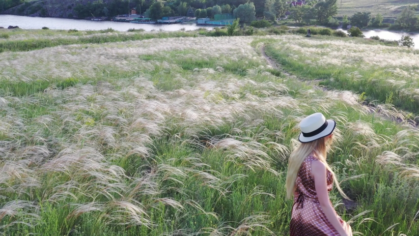 Beautiful girl in dress and hat on the field in the setting sun.