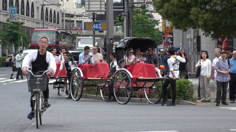 ASAKUSA,  TOKYO,  JAPAN - CIRCA MAY 2019 : Rickshaw puller and tourist. Guided tour on rickshaw is a popular style of sightseeing for tourists. It is also known as “jinrikisha (man powered vehicle)”.