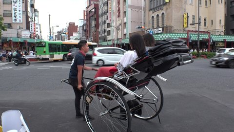ASAKUSA,  TOKYO,  JAPAN - CIRCA MAY 2019 : Rickshaw puller and tourist. Guided tour on rickshaw is a popular style of sightseeing for tourists. It is also known as “jinrikisha (man powered vehicle)”.