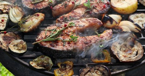 Grilled fish, grilled salmon steak with the addition of rosemary, aromatic spices and vegetables on the grill plate outdoors, close-up, 4k. Grilled seafood