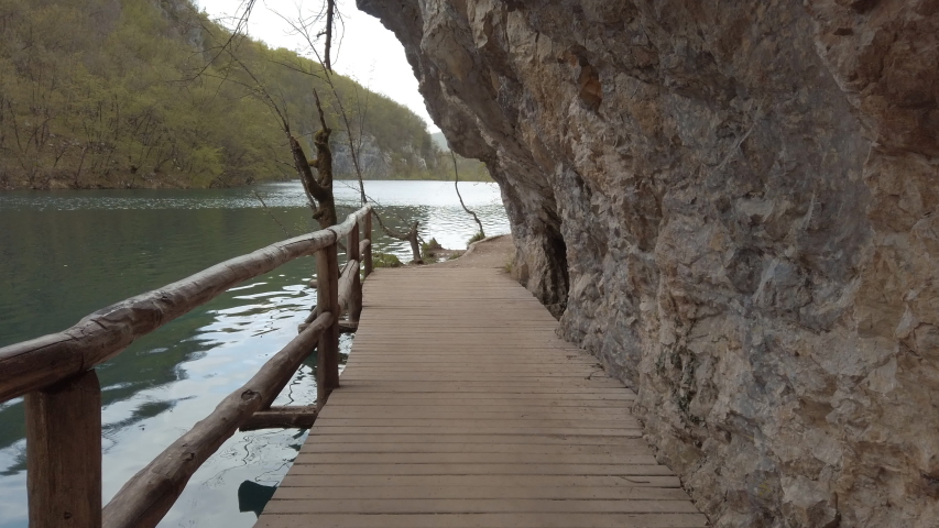A man made wooden footpath between a clear blue lake and mountain cliff side