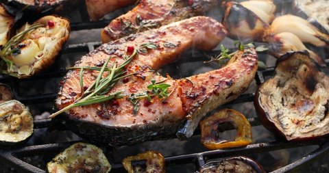 Grilled fish, grilling salmon steak with the addition of rosemary, aromatic spices and vegetables on the grill plate outdoors, close-up, 4k. Grilled seafood