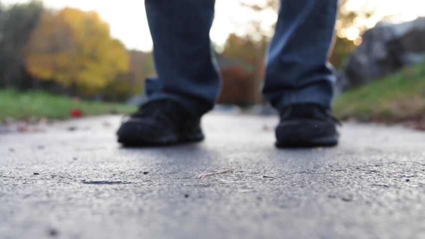 Low Angle Close Up of Dropped Falling Red Rose Flower on Asphalt Trail and Male Legs Walking Away From Scene Expressing Displeasure