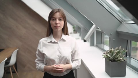Young beautiful business girl scolding someone and gesticulating with hands against the dormer windows in a bright office. 4K UHD