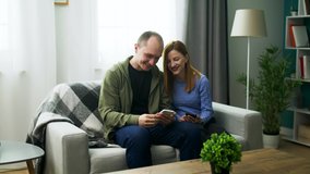 A young couple watching a fun video on a smartphone in their cozy living room