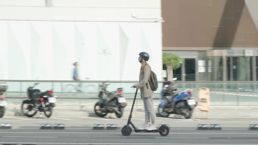 Young female with backpack riding Electric Scooter in the downtown wearing glasses and balck helmet 