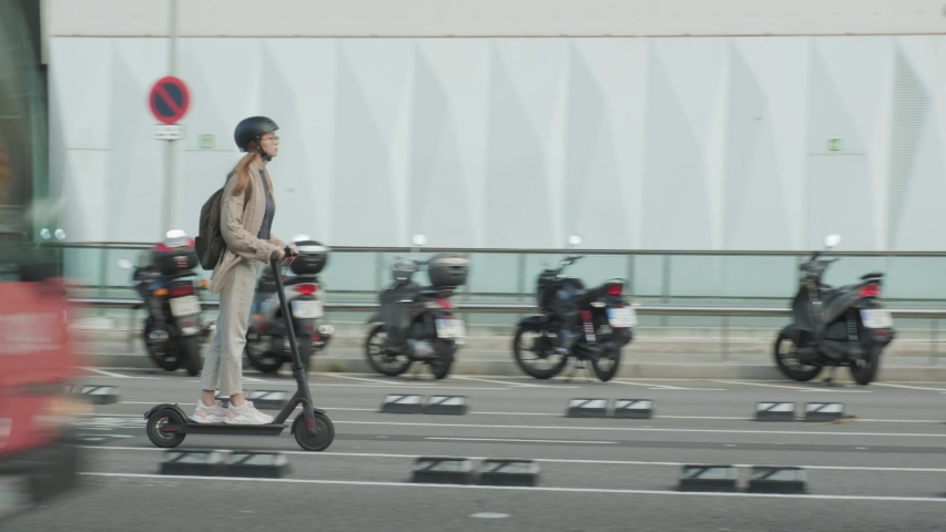 Young female riging Electric Scooter along the street and a bus passing in front   | Shutterstock HD Video #1030319357