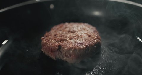 Chef preparing the burger, frying the meat with melted cheese on the pan. Frying cheeseburger meat on iron plate. Slow motion close up