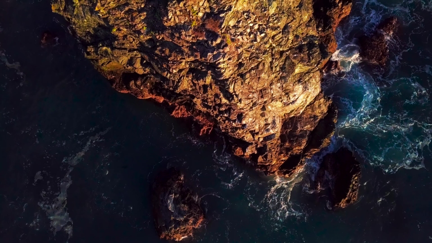 Rising aerial view of rocky cliffs and foaming ocean waves at sunset in Big Sur California