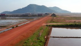 Aerial drone footage moving forward above a road surrounded by salt field near Kampot in Cambodia.