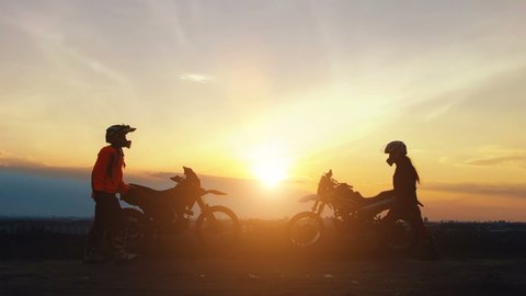 Silhouettes two riders with their bikes greet each other with victory. Silhouettes of motorcycles and riders on the background of beautiful sunset. Enjoy the freedom. Enduro.