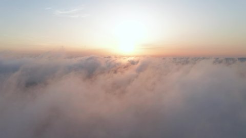Moving white clouds blue sky scenic aerial view. Drone flies high back in blue sky through the fluffy clouds in the evening at the bright sun. Sun is hidden behind the clouds at sunset the fog. Nature