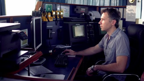 Marine navigational officer during navigational watch on Bridge . He works with paperjob on the computer. Modern work at sea