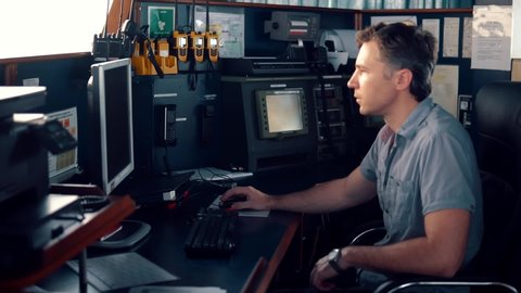 Marine navigational officer during navigational watch on Bridge . He works with paperjob on the computer. Modern work at sea
