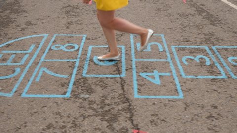 Young adult woman just jump at hopscotch court, tracking camera show only legs and pavement with painted numbered squares