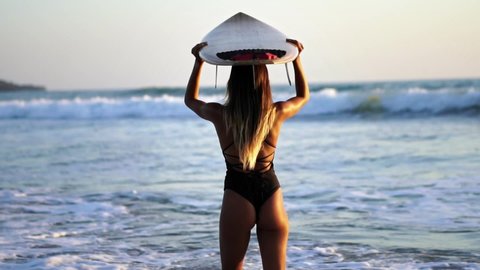 Rear view of attractive surfer girl model walking on beach with surfboard low angle of woman ass, slow motion. Healthy Active Lifestyle. Surfing, Fashion. Summer Vacation. 