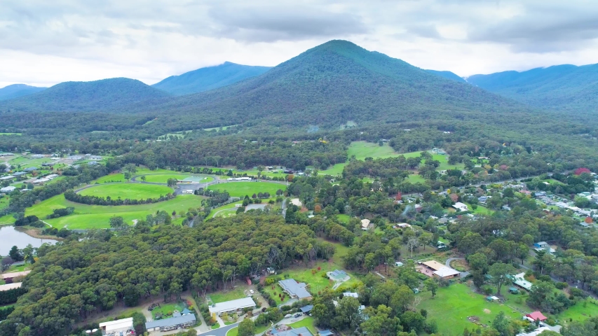 Slow aerial descend over rural luxury houses facing forested hill and mountains in Healesville, Australia