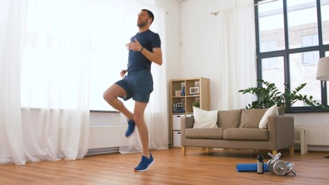 fitness, sport, technology and healthy lifestyle concept - man with wireless earphones running on spot at home