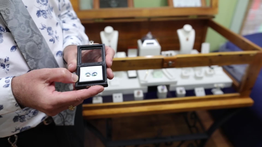 In a jewellery shop, a sales associate showing a box which has a white stone to lady customer nearby him