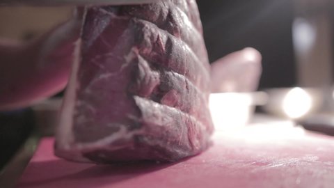 In a hotel, chef cutting the top portion of the meat placed on the pink cutting board using a sharp knife