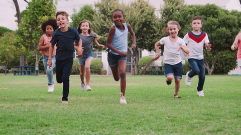 Group Of Excited Children Playing With Friends And Running Across Grass Playing Field