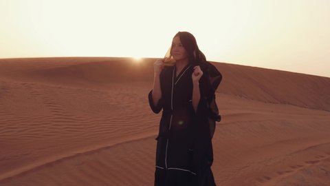 Portrait of a young Arab woman wearing traditional black clothing during beautiful sunset over the desert.