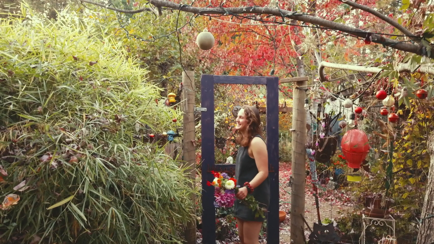 Woman with a bouquet walks through gate and winks. Gate says "life