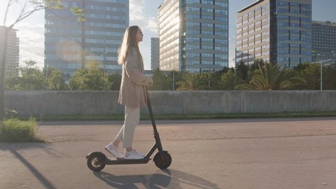 Young beautiful woman riding an electric scooter to work, modern girl, new generation, electric transport, ecology, ecological transport, sunset, electric skateboard, 4k