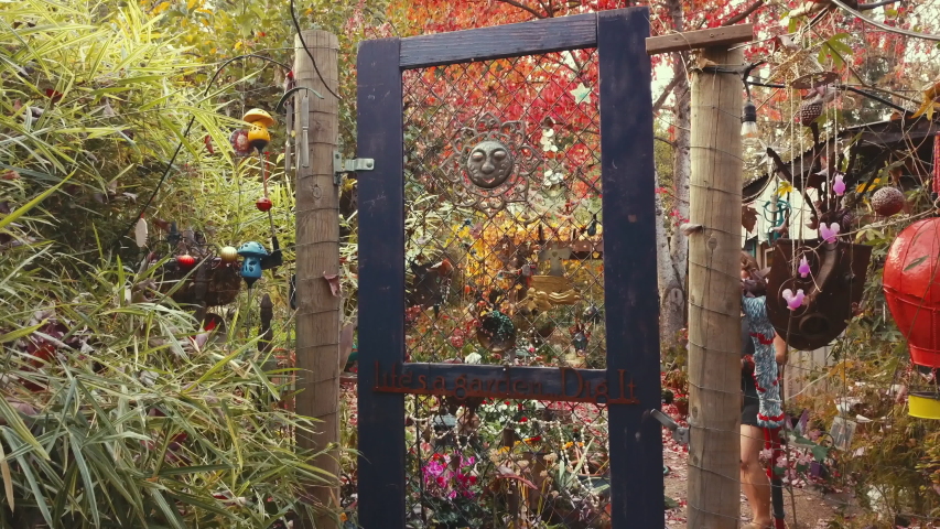 Woman with a bouquet walks through gate and winks. Gate says "life's a garden, dig it"