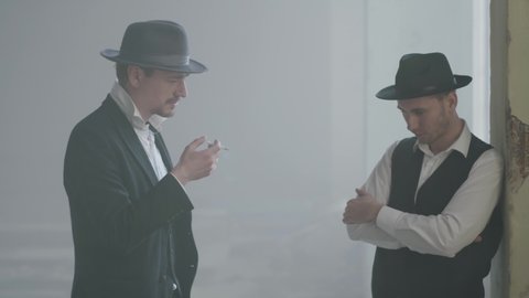 Two confident adult men in fedora hat standing in the broken durty place and talking. Abandoned dilapidated building. Self-confident businessman relaxing. Mafia clan. Criminal grouping.