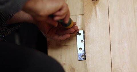 Carpenter work- screwing a door hinge. Close up view of craft working with  hand screwdriver and wooden door