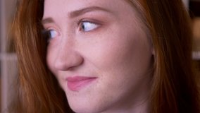 Closeup portrait of young cheerful redhead caucasian female student looking at camera smiling with shyness in the college library