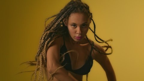 Expressive woman with afro dreadlocks dancing in studio. Portrait african american woman performing modern dance on yellow background. African girl dancing in slow motion