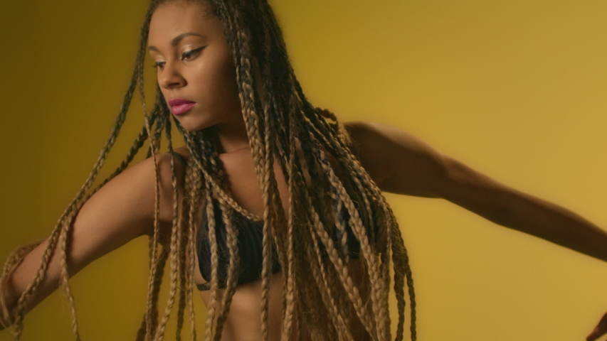 Black woman dancing on yellow background. Portrait african woman dancing in studio. Afro girl with dreadlocks dancing in slow motion. African ethnicity dancer. Motion in modern dance concept