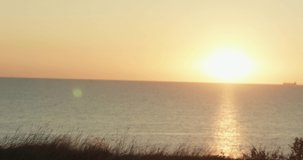 A cute young woman in white dress walks on the edge of a cliff and enjoys the sunset. Against on background of sea sunset. 4K video.