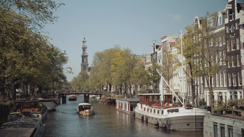 4K UHD - Prinsengracht, Amsterdam, The Netherlands (Holland). Boats going over the dutch canals, near leidseplein and dam square. Westerkerk (Westertoren) in the background. Canal tours in summer.