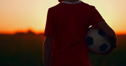 Boy holding a soccer ball standing at sunset in the field