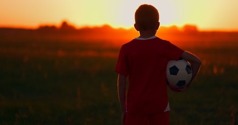 boy with a ball in a field at sunset, boy dreams of becoming a soccer player, boy goes to the field with the ball at sunset