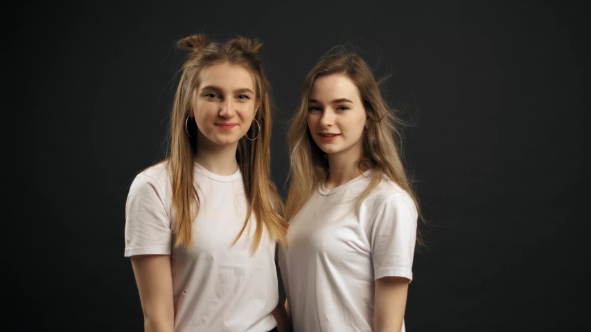 Two little girls are showing the heart with heir hands, smiling and looking at the camera. Black background in the studio. 4K slow motion shot