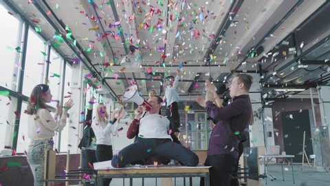 Manager start to dance on the table, sings into a megaphone, accelerates and slide on lap. Colleagues blow up flappers with confetti. Office celebration. Success. Corporate party business team