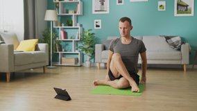 A young man studies yoga using instructions on a tablet