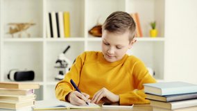 cheerful kid writing in notebook, smiling and showing thumb up at home