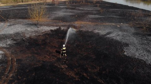 Brave Firefighter Sprays Burnt Grass with Water. Concept of Extinguishing a Wildfire