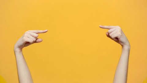 Woman hands pointing on copyspace isolated over yellow orange background in studio. Copy space for advertisement. With place for text or image promotional content. Advertising area, workspace mock up.
