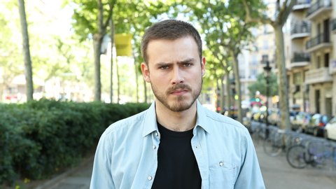 Front view portrait of a casual angry man looking at camera in the street