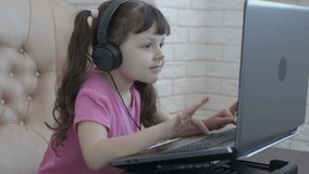A child with headphones playing on the computer.  Happy little girl playing video game.