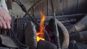 Blacksmith working with blacksmith furs in forge. Hot metal part in fire, then on stithy.